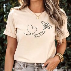 Spread kindness wherever you go with our "Bee Kind" Shirt! Featuring an adorable bumble bee flying around a heart, this motivational tee is a perfect reminder to choose kindness every day. Whether you're a nature lover or simply want to inspire positivity, this shirt is a perfect addition to your wardrobe. This bumble bee shirt is made with a soft cotton and a quality print that will have you fall in love with it over and over again. This Premium crafted t-shirt features a crew neck, short sleev Be Kind Tshirt, Bee Flying, Bee Shirt, Choose Kindness, Bee Kind, Spread Kindness, Save The Bees, Art Shirts, Look Plus