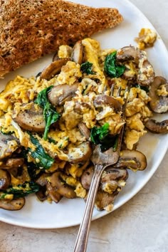 an omelet with mushrooms and spinach on a plate next to a slice of bread