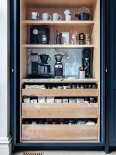 an open cabinet with coffee maker and cups on it's shelves in a kitchen