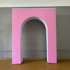 a pink arch sitting on top of a hard wood floor next to a gray wall