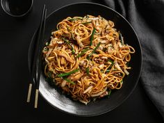 a black plate with noodles, mushrooms and green onions on it next to chopsticks