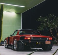 a red sports car parked in front of a building with green walls and plants behind it