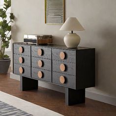 a room with a dresser and lamp on the sideboard next to a large potted plant