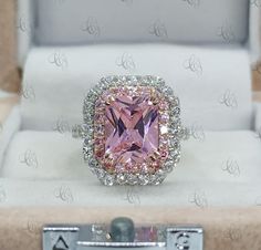 a pink diamond ring sitting on top of a white box with silver trimmings