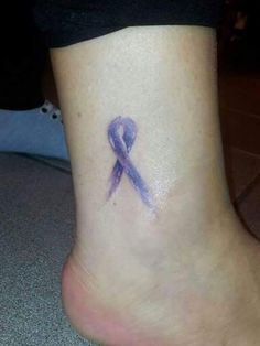 a small purple ribbon tattoo on the side of a woman's foot, which has been