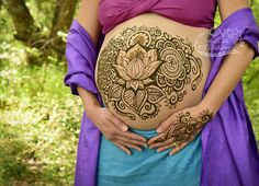 a pregnant woman with henna tattoos on her belly in the woods, holding her stomach