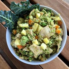 a white bowl filled with food sitting on top of a wooden table next to a leaf