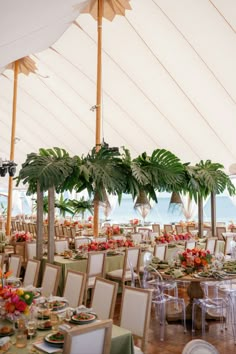 tables and chairs are set up in a tent with palm trees on the beach behind them