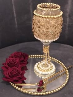 a glass candle holder sitting on top of a table next to red roses and a pair of scissors