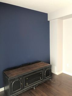 an empty room with blue walls and a black entertainment center in the corner on hardwood flooring