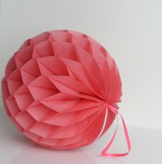 an origami ball on a white surface with pink ribbon tied around it,