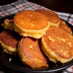 some pancakes are stacked on top of each other in a black plate with red and white checkered tablecloth