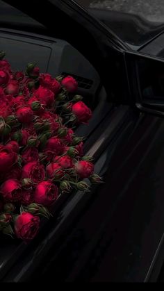 a bunch of red roses sitting on the hood of a black car with it's door open