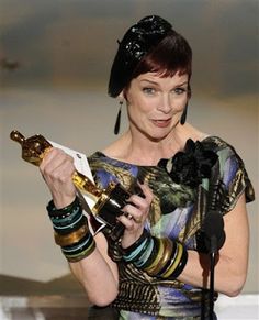 a woman holding an award in front of a microphone and wearing a black headdress