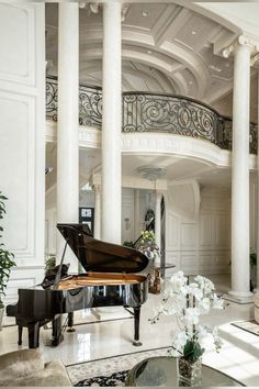 a grand piano in the middle of a living room with white walls and columns on either side