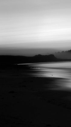 a black and white photo of the ocean at dusk with fog in the sky above