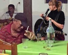 a man sitting at a table with a guitar next to a woman singing into a microphone