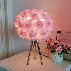 a pink lamp sitting on top of a white table next to flowers and a potted plant