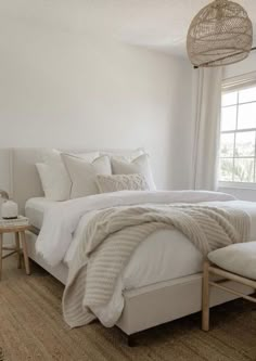 a bed with white linens and pillows in a bedroom next to a large window