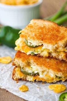 two grilled cheese sandwiches stacked on top of each other with green peppers and jalapenos in the background