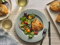 a plate with meat and salad on it next to two glasses of wine, silverware and utensils