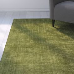 a green rug in the middle of a living room with a chair and window behind it