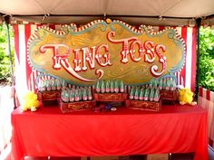 a red table topped with lots of bottles under a sign that says ring toss