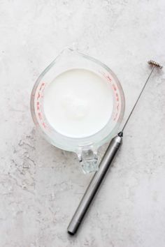 a glass measuring cup with a screwdriver next to it on a white surface