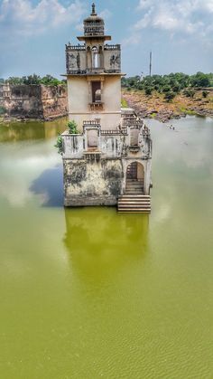 an old tower sitting in the middle of a body of water with stairs leading up to it