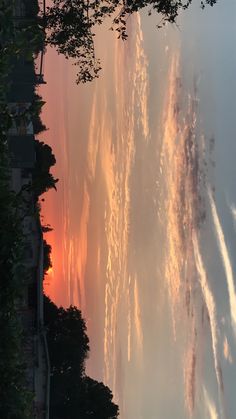 the sun is setting behind some trees and clouds in the sky over water with jets coming from them