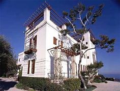 the house is white and has brown shutters on the front, and two balconies on the second floor