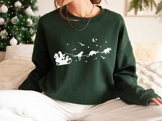 This fun Christmas sweatshirt features dinosaurs pulling santa's sleigh. You'll love wearing this fun crewneck during the festive season, or anytime! Makes a great gift for any dino lover. * Q U I C K * F A C T S * ♥ 50% cotton / 50% poly fabric blend ♥ Design is high quality digital print ♥ Washed on cold and air dried is best, but regular/washing and drying is fine as well! * S I Z I N G * ♥ Sizing is unisex so runs like men's, though not overly large ♥ Most women find their typical size works Winter Dinosaur Print Crew Neck Top, Cat Core, Dinosaur Sweater, Dino Shirt, Cat Dad Gifts, Santa's Sleigh, Cat Sweater, Dinosaur Gifts, Cat Mom Gifts