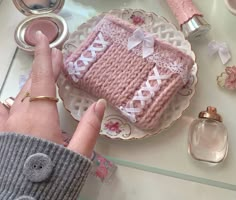 a hand is holding a pink knitted object on a plate with other items around it