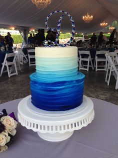 a wedding cake with blue and white frosting sitting on top of a table under a tent