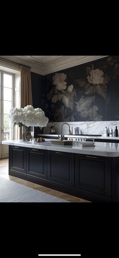 a large kitchen with black cabinets and white flowers on the counter top, along with an open window