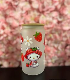 a hello kitty glass jar with strawberries on it and flowers in the back ground