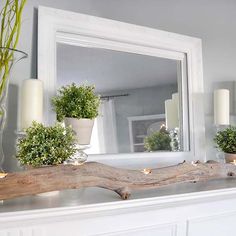 a fireplace mantel with candles and plants on it, in front of a mirror