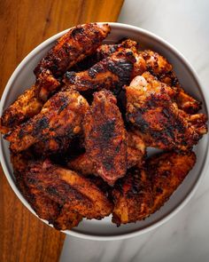 a white bowl filled with chicken wings on top of a wooden table