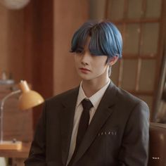 a man with blue hair wearing a suit and tie sitting in front of a desk