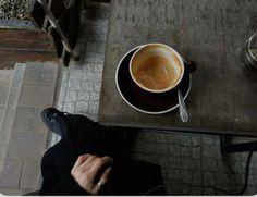 a cup of coffee sitting on top of a table next to a person's feet