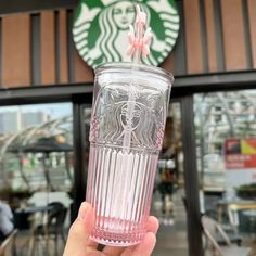 a person holding up a pink glass in front of a starbucks