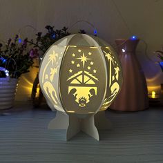 a light up ball with a nativity scene on it sitting on a table next to some flowers