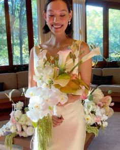 a woman in a white dress holding a bouquet of flowers and smiling at the camera