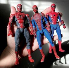 three spider - man action figures are posed in front of a person's hand