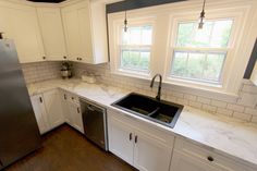 a kitchen with white cabinets and marble counter tops, stainless steel refrigerator and dishwasher