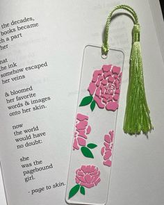 a bookmark with pink flowers and green tassels on top of an open book