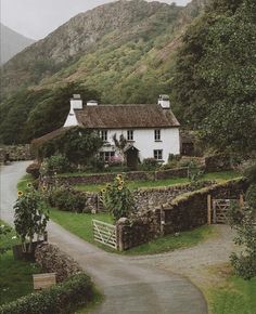 a white house sitting on the side of a lush green hillside next to a road