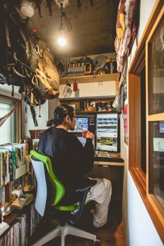 a person sitting at a desk with a computer in front of him and lots of clutter on the wall