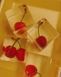 four pieces of ice with cherries in them sitting on a yellow tray next to each other