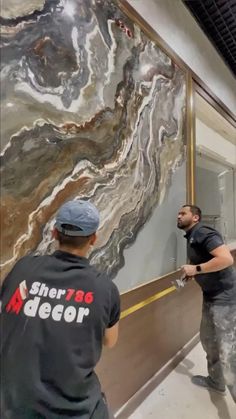 two men in black shirts are painting a large marbled wall with gold trimming